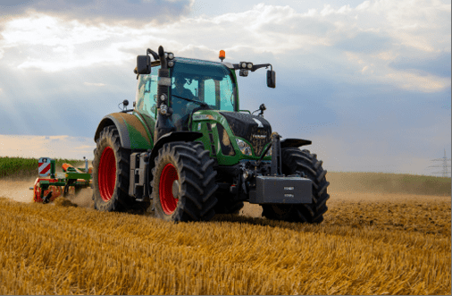 A green tractor harvesting crops from a field, demonstrating the use of IoT in Agriculture.