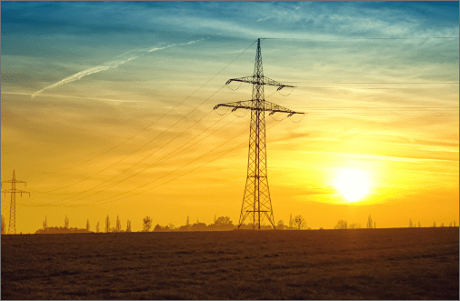 An electric transmission tower with the sun setting in the background behind it demonstrating Airgain's participation in the Energy industry.